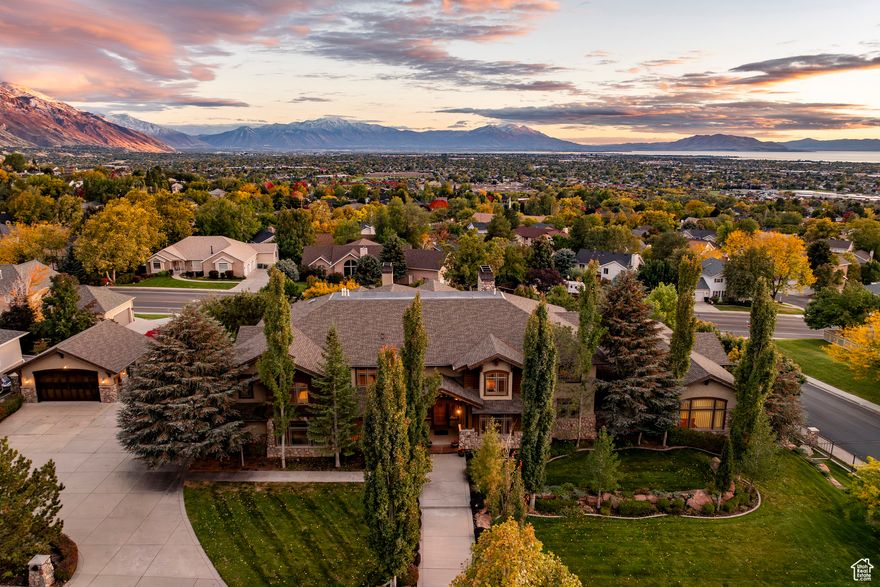 This remarkable lodge-style home in Lindon sits above the valley with impressive views of Utah Lake and the surrounding mountains. With nearly 17,000 square feet, it offers exceptional space for both everyday living and large gatherings. The main level centers around a spacious great room highlighted by a massive stone fireplace and large timber beams, with doors that open to a generous deck overlooking the valley and lake. The kitchen and dining areas are open and inviting, designed for entertaining and connection. There are ten bedrooms, multiple family rooms, and comfortable spaces for both relaxation and recreation. The home includes an indoor basketball court, an exercise room, a game room, a resort-style swimming pool, an additional detached garage, and beautiful outdoor areas with mature trees that take full advantage of the setting. Every aspect of the property reflects a sense of scale, comfort, and livability that is hard to find. It is a rare opportunity to own a home that blends mountain architecture with modern function and lifestyle in one of the most desirable areas of Utah County.
