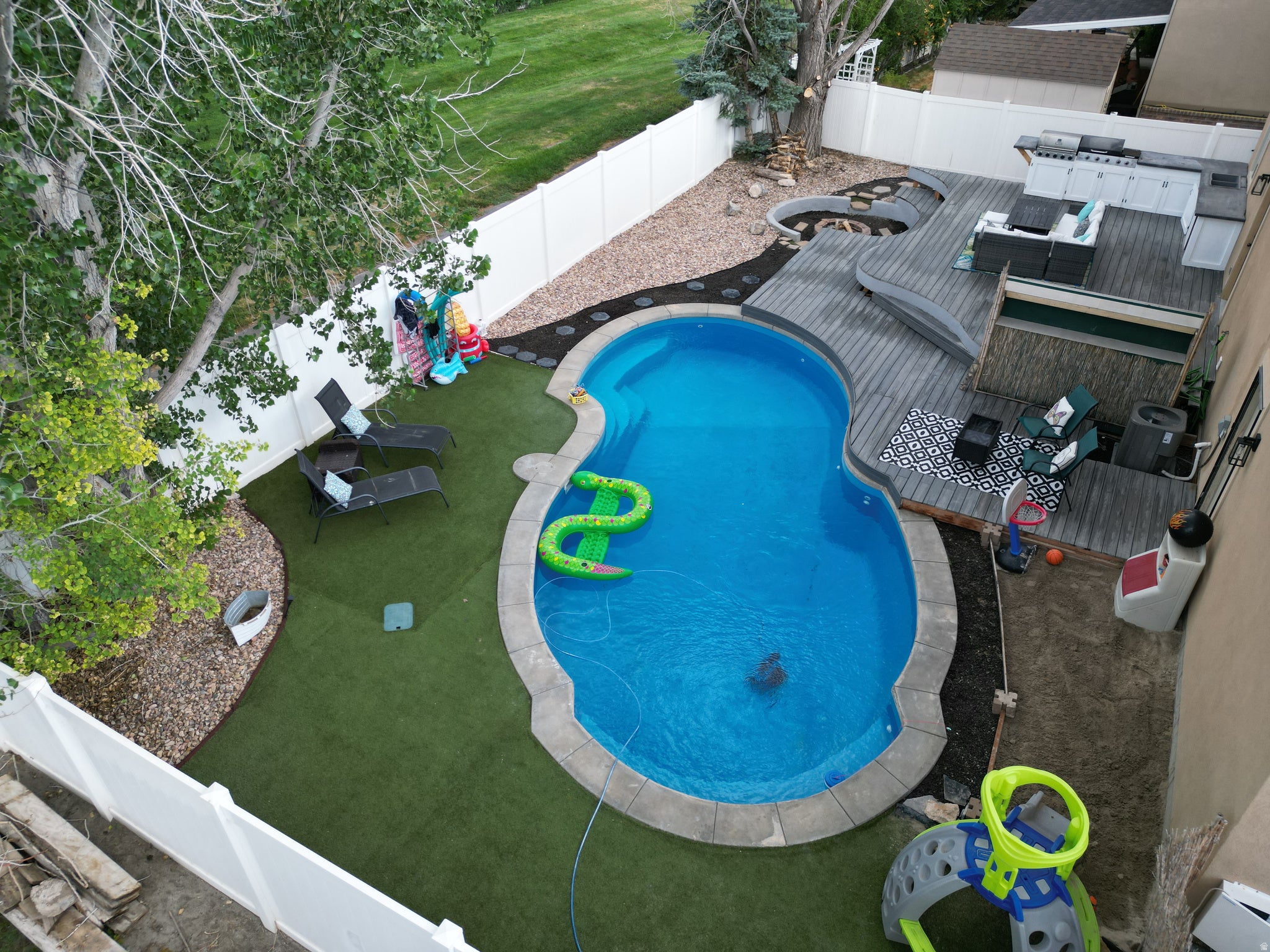 Backyard oasis featuring a custom-shaped swimming pool with stone coping, a multi-level composite deck, an integrated outdoor kitchen, and a circular fire pit area