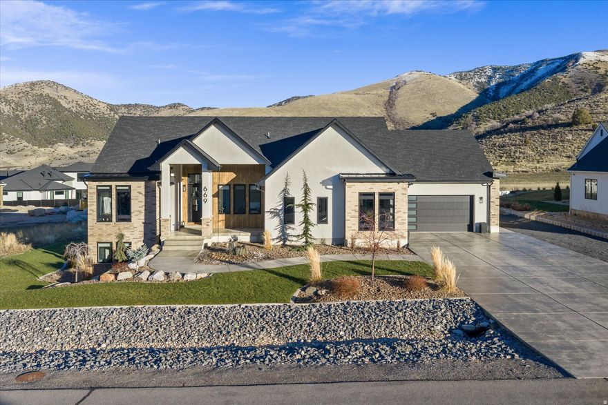 This beautiful custom build is perfectly situated in the idyllic town of Mantua, offering breathtaking mountain views, small-town charm, and easy access to outdoor recreation.  Step inside to find spacious open-concept living with high-end finishes throughout. The main level features a gourmet kitchen with custom cabinetry, quartz and honed black granite countertops, commercial fridge and freezer, a top of the line gas range, and a large island-perfect for entertaining. The attached butlers pantry boasts extra storage and prep space, along with double wall ovens.   The adjoining great room features 12 ft ceilings, engineered hardwood floors, and a cozy fireplace, creating the perfect gathering space. Large black Andersen casement windows let in natural light and gorgeous mountain views. Walk through the sliding doors to the oversize deck to take the views in more fully. Home is equipped with a full audio system, including outdoor areas.   The luxurious primary suite offers a private retreat complete with a spa-style bathroom, dual vanities, a soaking tub, and a walk-in shower. The large walk-in closet also features a roomy separate laundry room.   The lower level features a homey living area, tall 9 ft ceilings, game table/dining area, as well as a built-in wet bar with a microwave. Downstairs there are also 3 bedrooms, 1.5 baths, a laundry room, a fully insulated cold storage room, and sliding glass doors to a large patio area.   Spacious 3 car garage has plenty of room for all your toys with an epoxied finish as well as a garage door in the back for easy access.   The private .61 acre lot features custom landscaping and a lovely water feature in the front and retaining in the back. The back is a blank canvas to finish how you'd like it. Want to add a pool? Gas and power are stubbed and ready.   Other features of the home include a whole home humidifier system, soft water, option for remote controlled shades, instantaneous hot water with tankless water heater, and power set up for a future hot tub.   Square footage figures are provided as a courtesy estimate only and were obtained from builder floor plans.  Buyer is advised to obtain an independent measurement. Agent related to Seller.