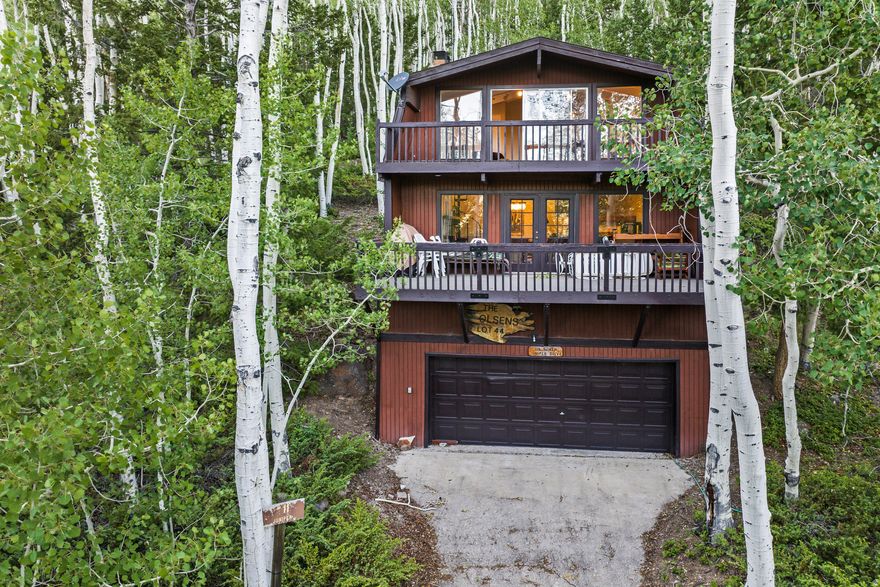 Rarely available rustic cabin located in highly sought after Fish Lake! This cabin has been enjoyed by the same family since it was built over 50 years ago.  Spacious, open floor plan with four bedrooms, one on the main floor  and three bathrooms. MVP flooring and newer paint throughout the main floor.  Large picture windows provide natural light and great views. Cozy wood burning fireplace adds comfort to the main floor living space.   Enjoy summer evenings on the spacious deck. Three additional bedrooms with vaulted ceilings and two additional bathrooms upstairs, all with newer carpet. Primary bedroom suite has a full bathroom, fireplace and its own private deck. Bonus two car built in garage which is rare for the area. Most furnishings are included in the sale.
