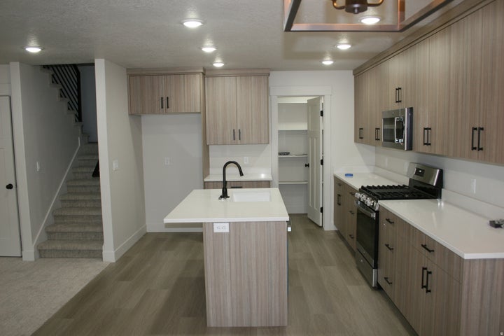 Modern kitchen featuring wood-finish cabinetry, stainless steel appliances, a center island with a sink, and white…