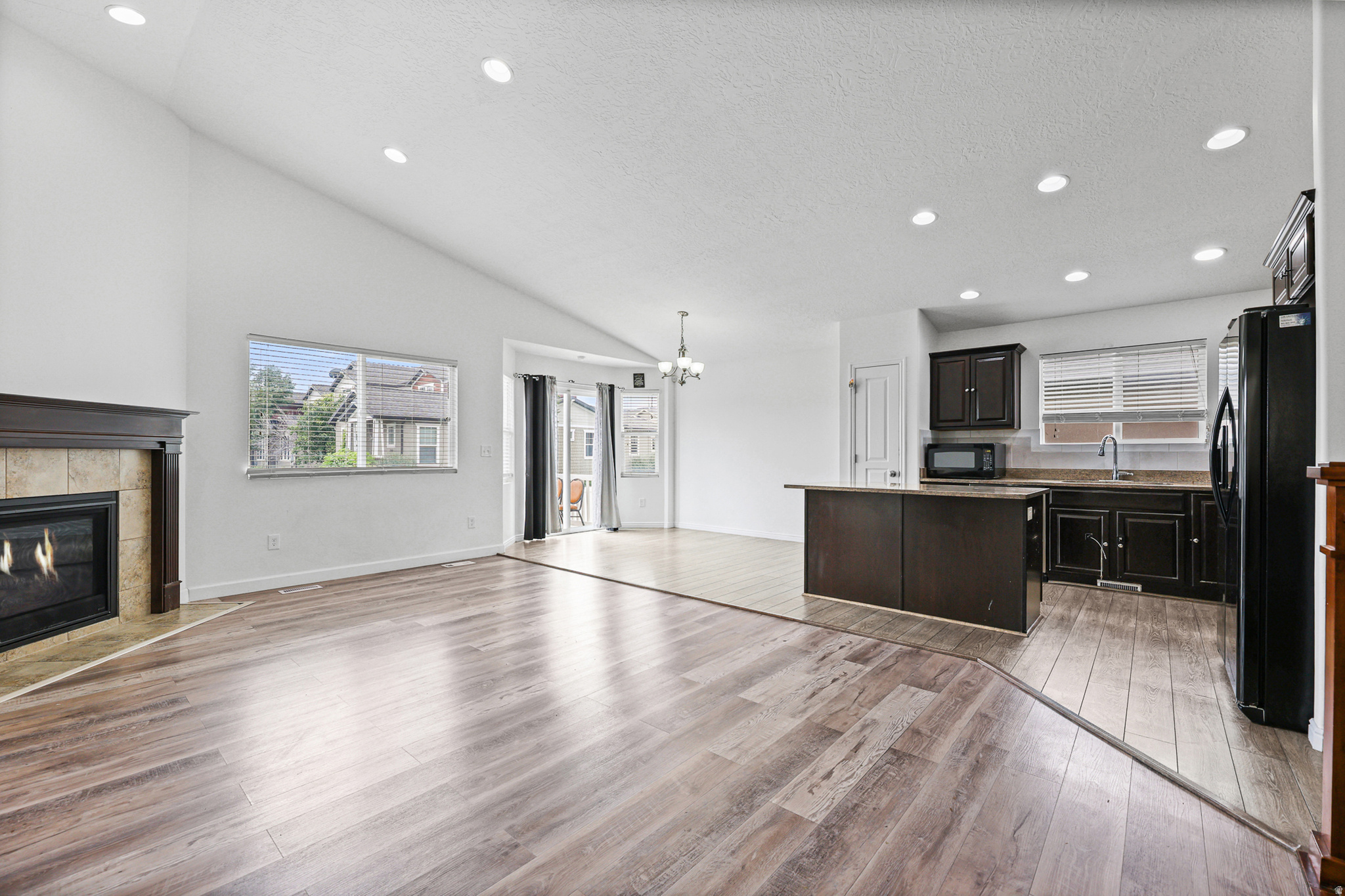 Bright living room with vaulted ceilings, large windows, and a gas fireplace that serves as a welcoming focal point. Sliding glass doors provide easy access to the backyard.