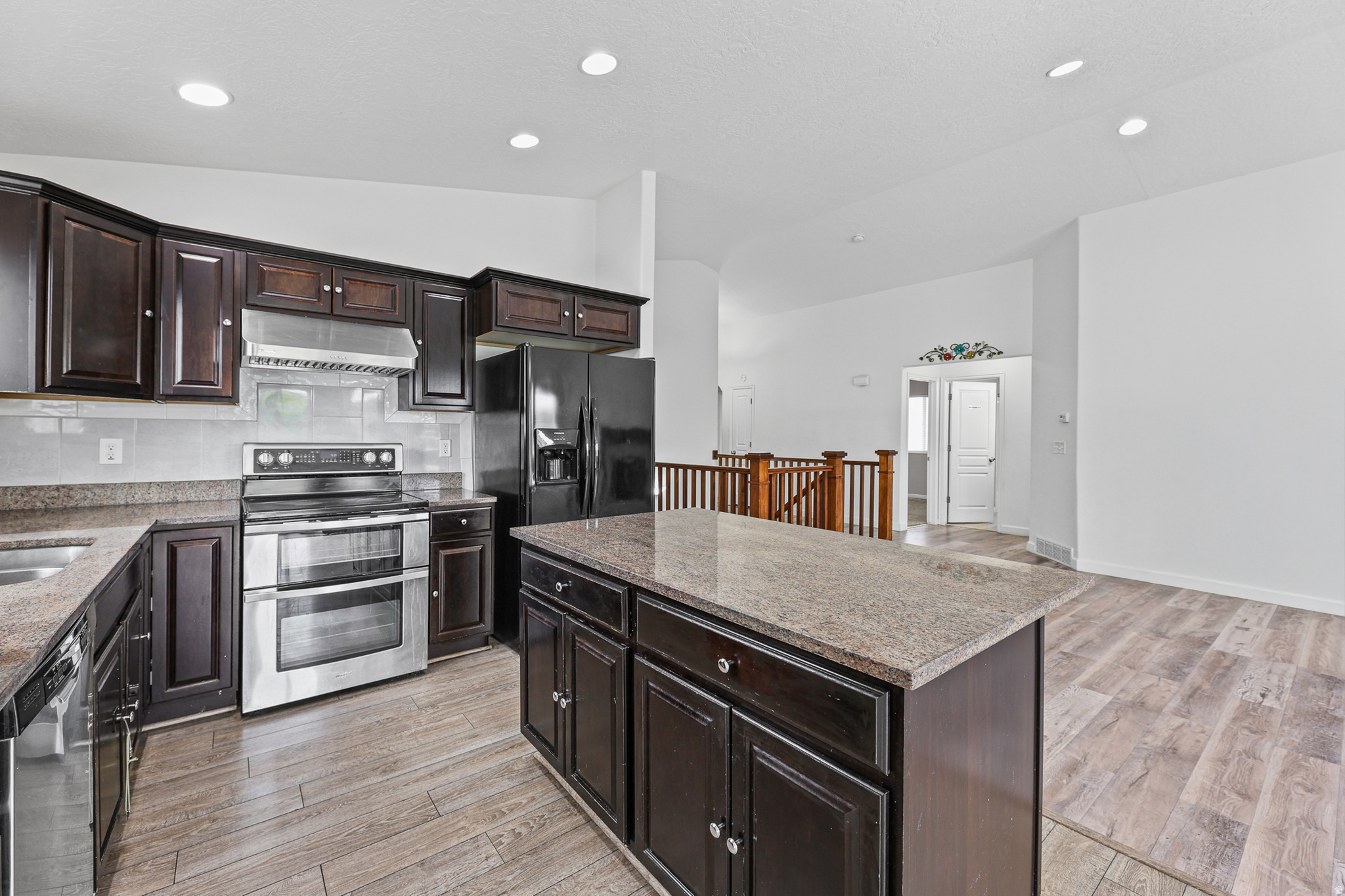 Open kitchen featuring a large center island, abundant dark cabinetry, stainless steel appliances, and generous workspace. The open layout connects seamlessly to the adjacent living and dining areas.