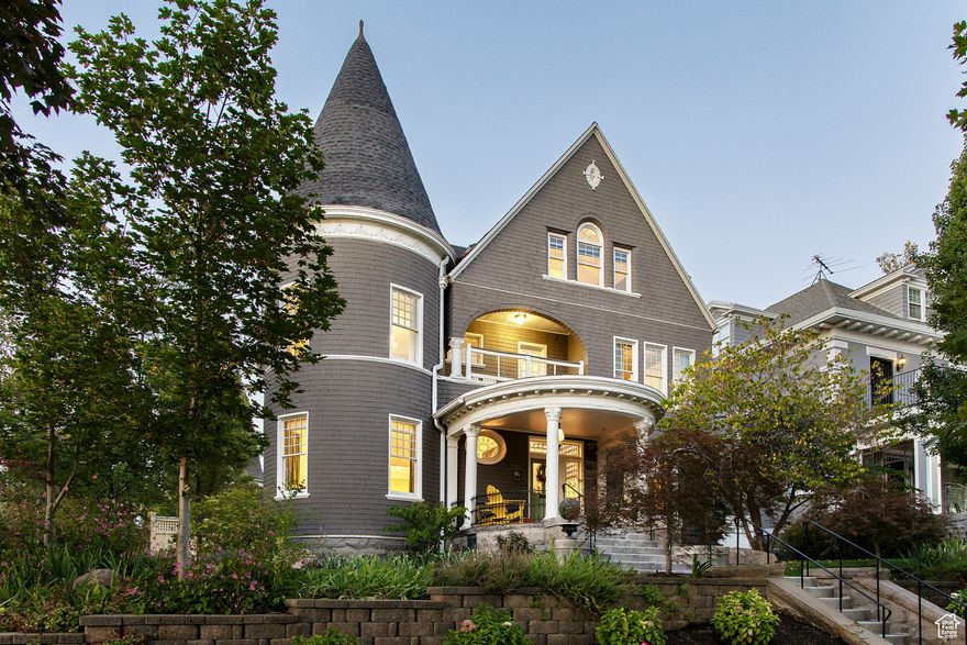 Set on one of Salt Lake City's most storied streets, this Utah Historic Registry home represents the best of classic architecture reimagined for modern living. Perfectly positioned on a quiet portion of this tree-lined stretch of East South Temple, this regal estate offers a rare blend of history, privacy, and refinement conveniently located near the University, downtown, and the city's cultural heartbeat. A gated, secure driveway tucked off a private lane ensures ease of access while maintaining a sense of seclusion. The home's stately columned front porch, mature trees, and master gardenerdesigned landscaping create a picture-perfect welcome, while its distinctive shingle siding evokes timeless East Coast elegance. Inside, the main level exudes warmth and character, with rich hardwood floors, exquisite millwork, and leaded glass windows. Pocket doors open to formal living and study spaces, and a charming powder bath with playful wallpaper adds a touch of whimsy. The formal dining room connects seamlessly to both the kitchen and living room, creating an ideal flow for entertaining. The renovated kitchen honors the home's heritage while incorporating modern convenience, featuring custom cabinetry, built-in storage, and a charming pantry hidden behind an original wood door. A new mudroom provides everyday functionality with direct access to the two-car garage and gated drive. Beyond the interior, the backyard is a private retreat designed for year-round enjoyment. A paver deck anchors the outdoor living space, complete with an outdoor kitchen, fireplace, and a covered lounge area outfitted with power, lighting, shades, and a ceiling fan, perfect for relaxation throughout the seasons. Fully gated and thoughtfully designed, the backyard offers room to dine, lounge, and play without interruption, creating a true extension of the home's living space. The second level is anchored by an inviting primary suite within the home's turret, offering a cozy reading nook framed by arched windows, a gas fireplace, and a marble-clad bathroom with dressing room, laundry, and balcony access. Additional bedrooms on this level include en suite baths, built-ins, and architectural details that capture the home's character. The third floor surprises with a sun-drenched office surrounded by walls of windows, framing views of the hillside and surrounding historic neighborhood. This level also features two additional bedrooms, each with charming window seats, built-ins, and their own private lofts, along with a full bath with dual vanity. The lower level reveals the home's rich history and incredible charm, with exposed brick walls, a gas fireplace, a cozy den, an original bank vault door leading to storage, and a spacious laundry room showcasing new mechanical systems. Every inch of this exceptional home reflects the thoughtful care and craftsmanship of its stewards. Beautifully landscaped grounds, a sense of privacy set back from the street, and the unique combination of architectural significance and modern ease make this a truly once-in-a-lifetime opportunity on South Temple.