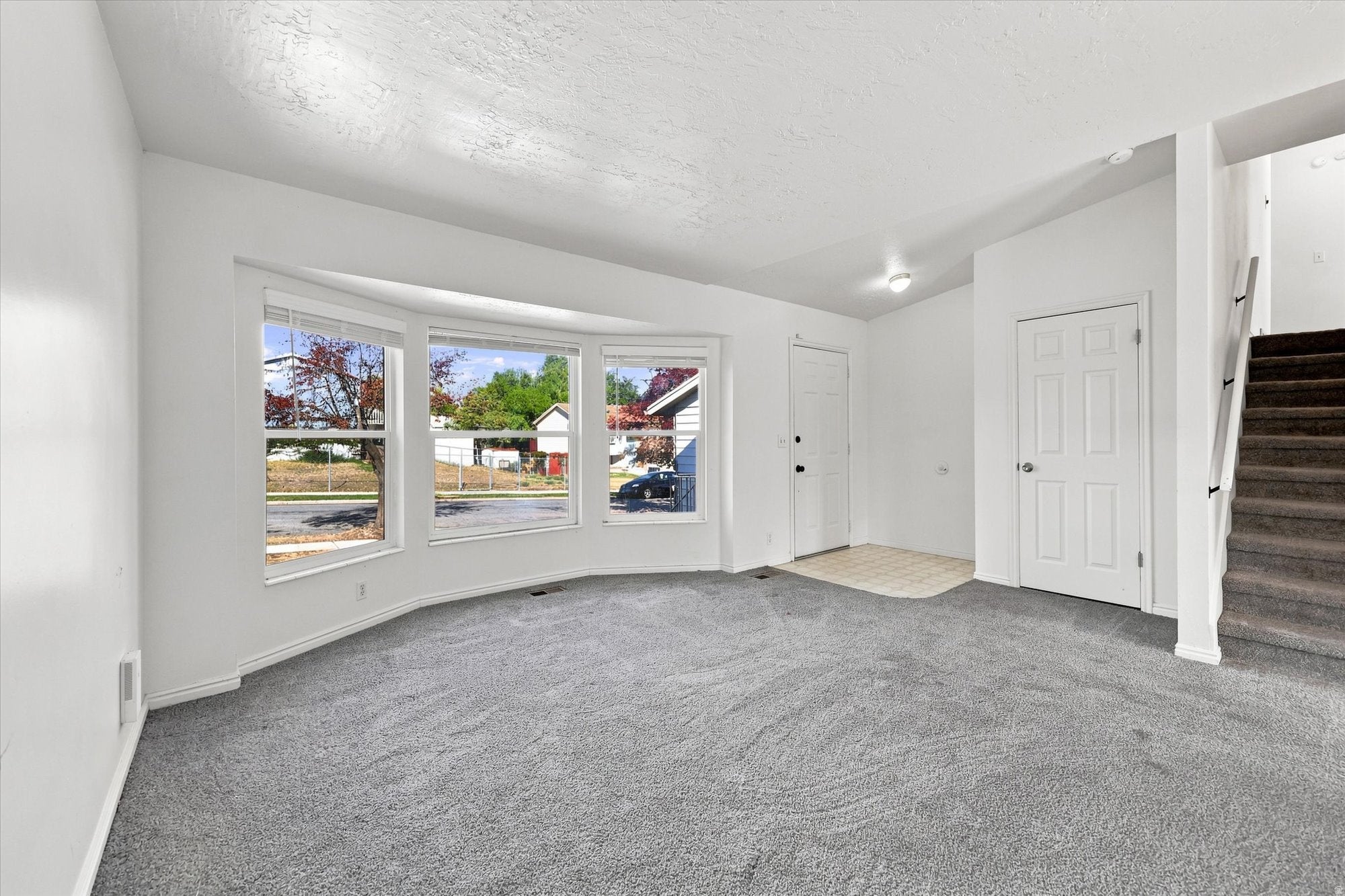Bright interior with a bay window, neutral carpeting, and a built-in staircase