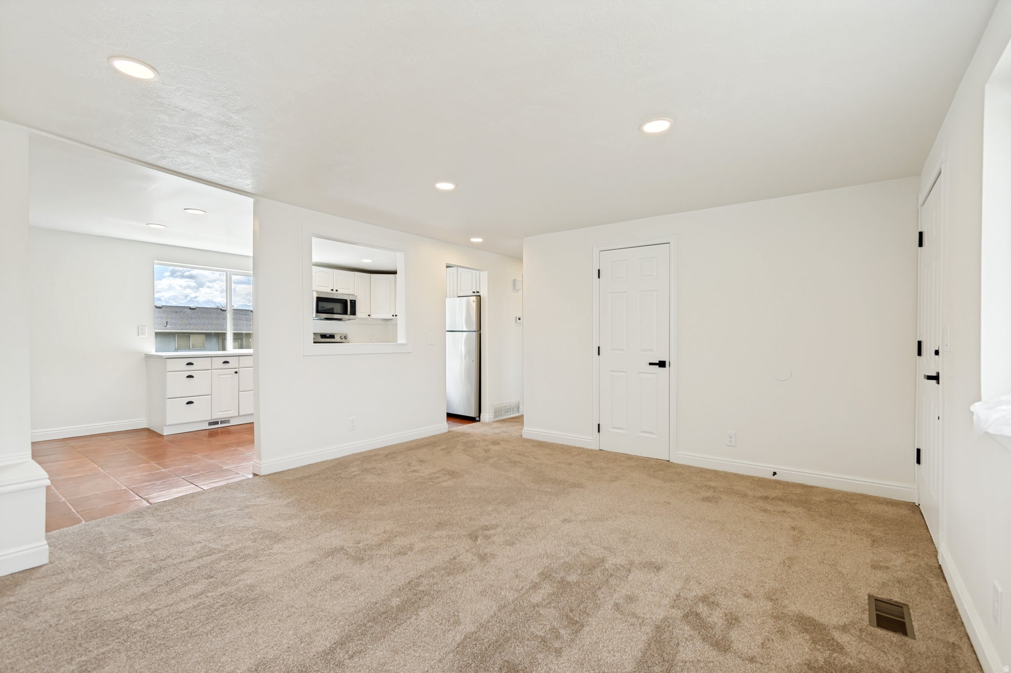 Recessed lighting, neutral carpeting, crisp white walls, and white paneled doors with matte black hardware
