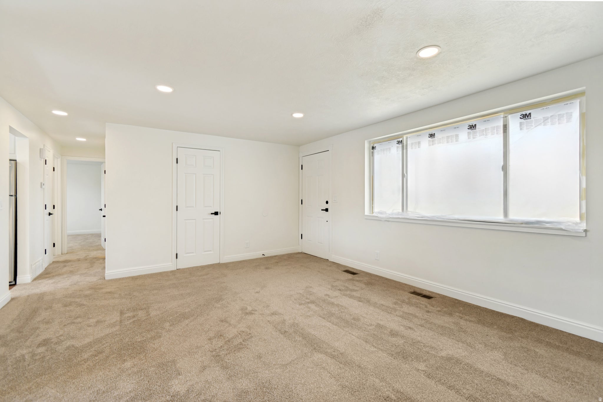 Recessed lighting, light beige carpeting, white walls, white trim, and white paneled doors with black hardware