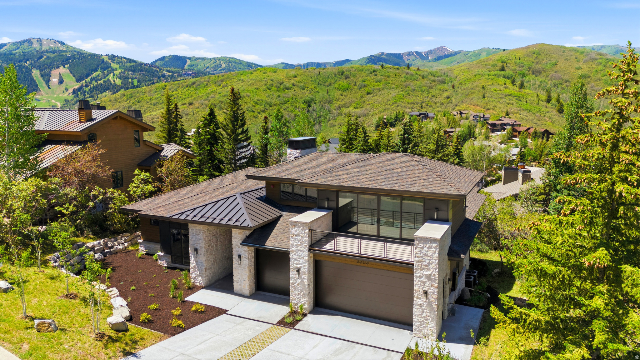 Modern architectural residence featuring stone facade accents, multiple garage bays, and an upper-level balcony