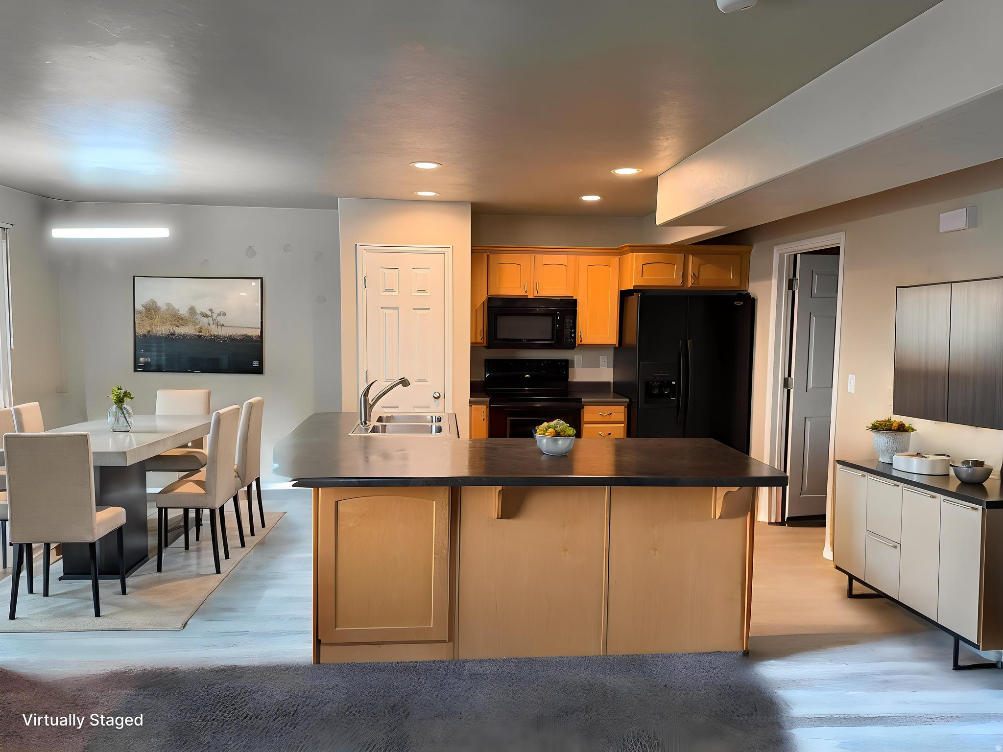 Kitchen island with integrated sink, black appliances, light wood-finish cabinetry, and recessed lightingVirtually modified