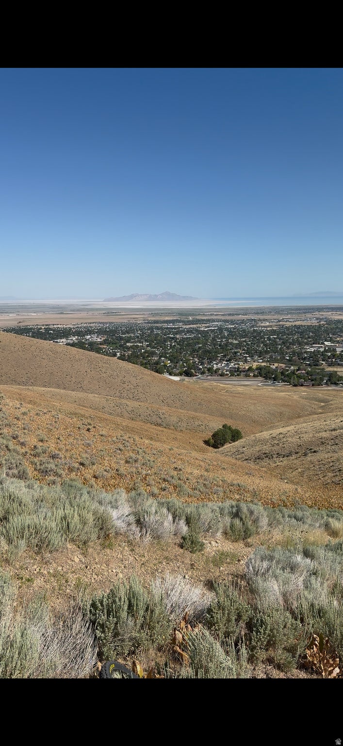 Expansive parcel featuring a sloped terrain with natural vegetation, offering distant city and mountain scenery under a clear sky