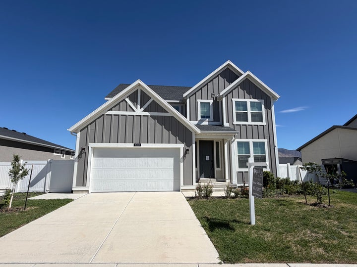 Two-story exterior with board and batten siding, attached garage, concrete driveway, and front lawn