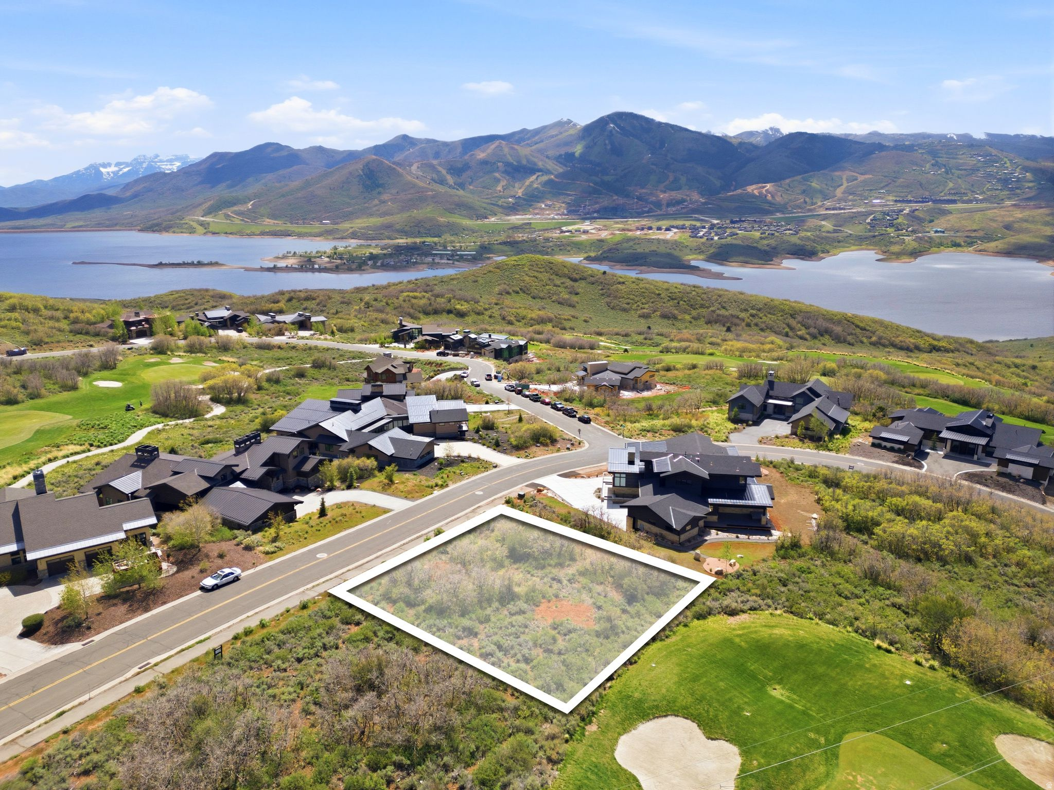 Elevated lot featuring natural vegetation, bordered by a paved road and a manicured golf course, with surrounding residences and distant water and mountain scenery