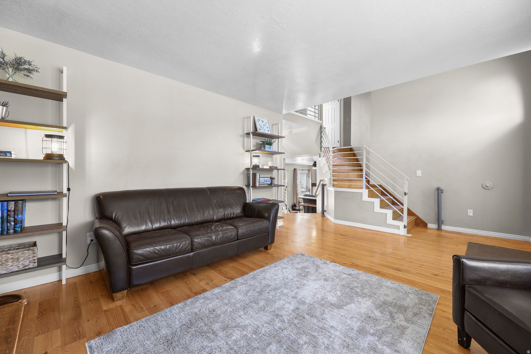 Open-concept living space featuring wood-finish flooring and a contemporary staircase with white metal railings