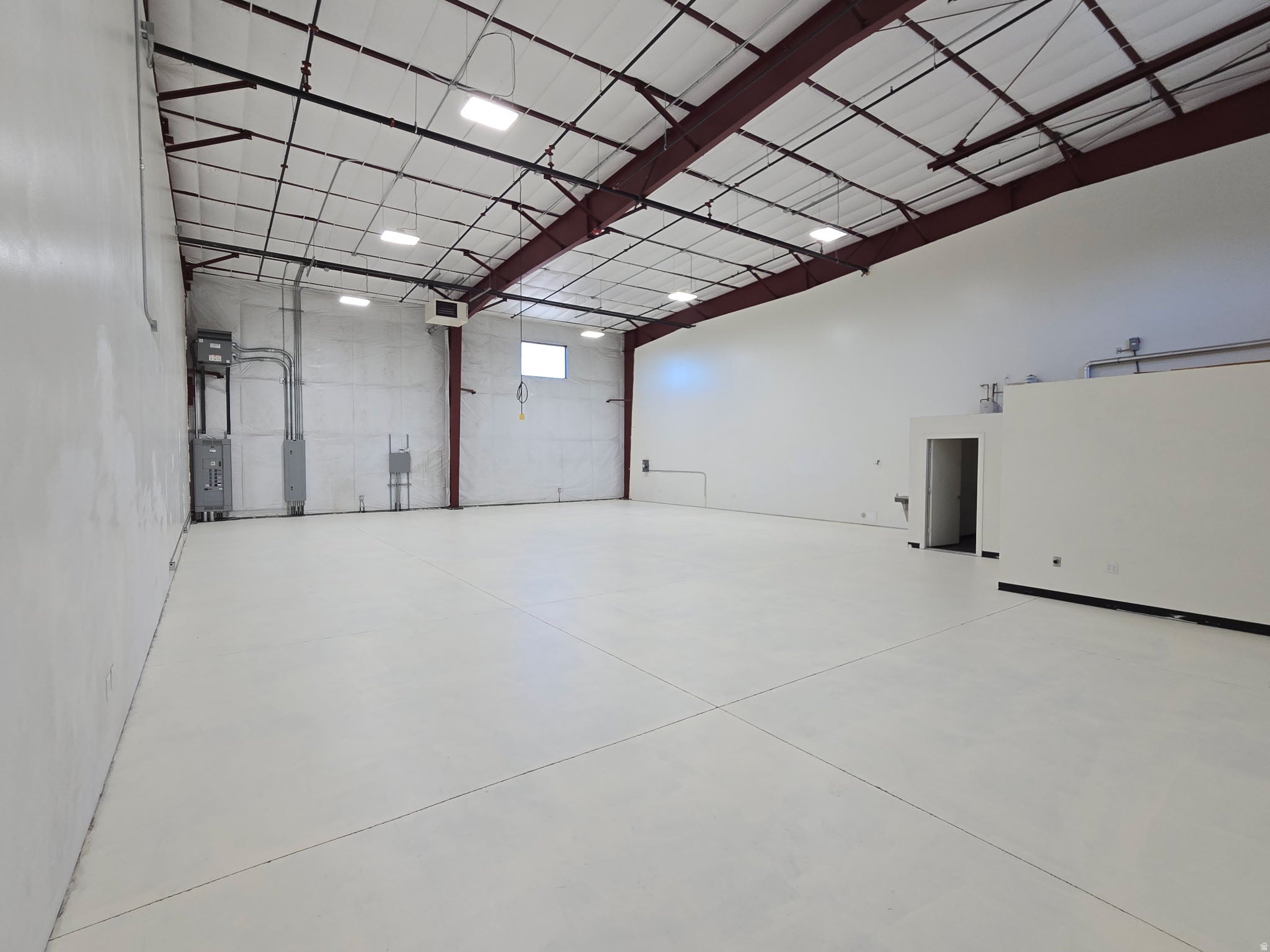 Expansive commercial space featuring a high ceiling with exposed structural beams, white-painted walls, and a light-colored concrete floor
