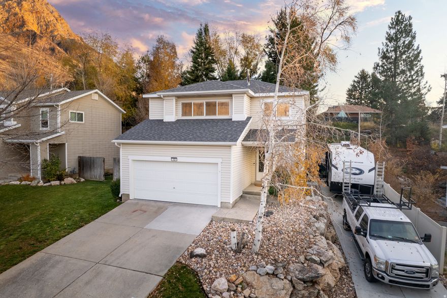 Tucked at the base of the Ogden mountains, this inviting two-story home offers a rare mix of privacy, scenery, and everyday comfort. Mature trees frame the terraced backyard, creating a natural retreat with views that stretch from the valley floor to the rugged face of Ben Lomond. Whether you're out on the patio or looking through the windows, the setting feels peaceful and grounded.  Inside, the main level opens into a generous great-room and kitchen-bright, connected spaces designed for easy living and gatherings. Stainless steel appliances and LVP flooring add a clean, modern feel, with soft carpet carrying up the stairs and into the bedrooms. A charming hidden nook beneath the staircase offers a fun surprise-perfect for a pet hideaway or clever extra storage.  Upstairs, the bedrooms are well-sized, and the home's thoughtful storage continues in the oversized crawl-space below-tall enough to stand in and ideal for keeping seasonal items neatly tucked away. A new roof and a recently installed AC unit offer added peace of mind.  Outside, the fenced yard and mountain backdrop make the space feel like its own escape. The property includes a two-car garage plus a separate RV pad and driveway, and the location sits within a quiet, secluded-feeling neighborhood with no through traffic.  Built in 1999 on a .17-acre lot, this home balances nature, function, and everyday comfort in a setting that feels truly special.