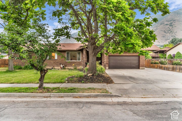 Single-story brick exterior featuring a wide concrete driveway, attached two-car garage, mature landscaping, and…