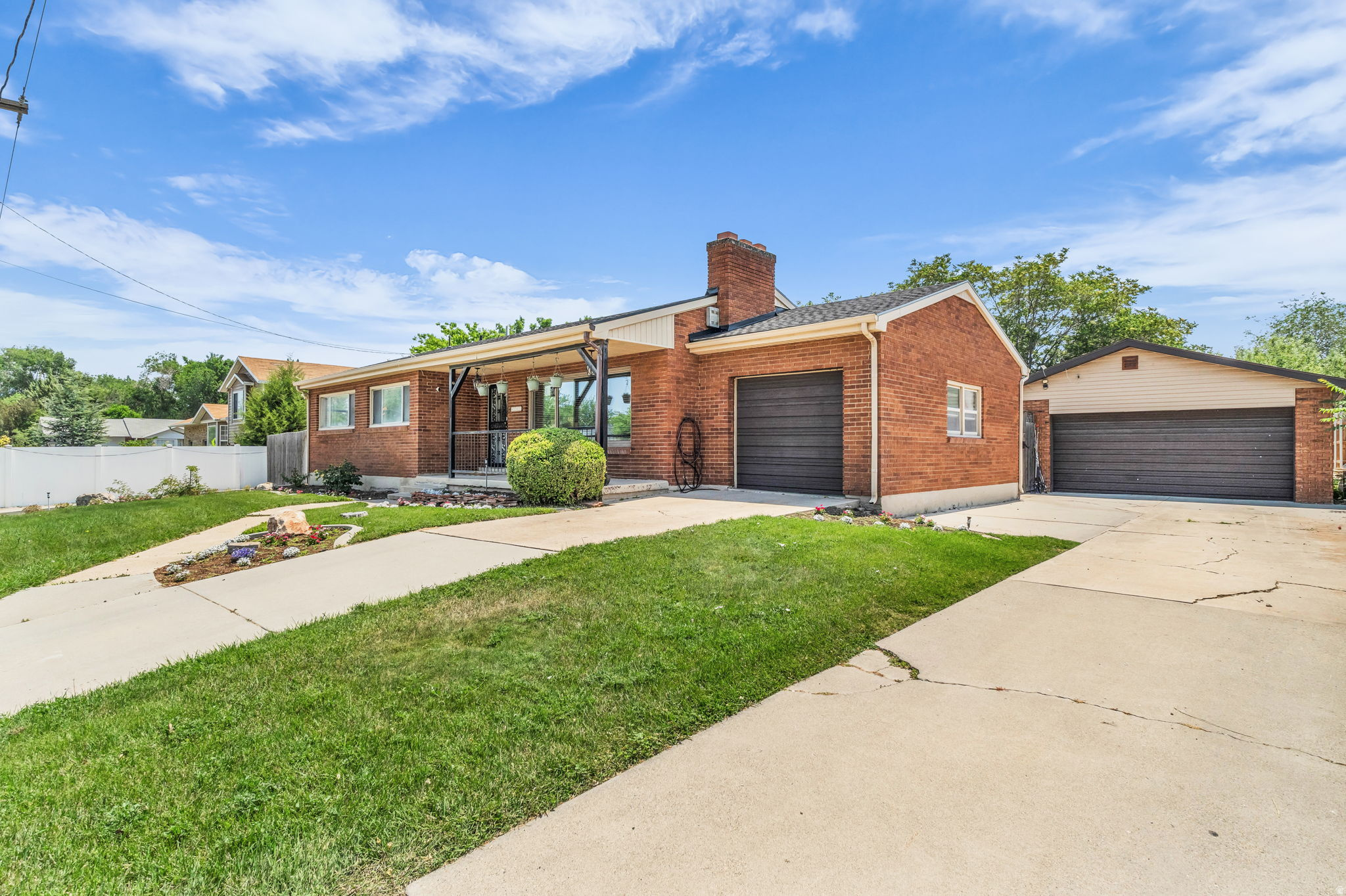Brick exterior with an attached garage, featuring a separate detached garage structure, paved driveways, a covered front entry, and a manicured lawn