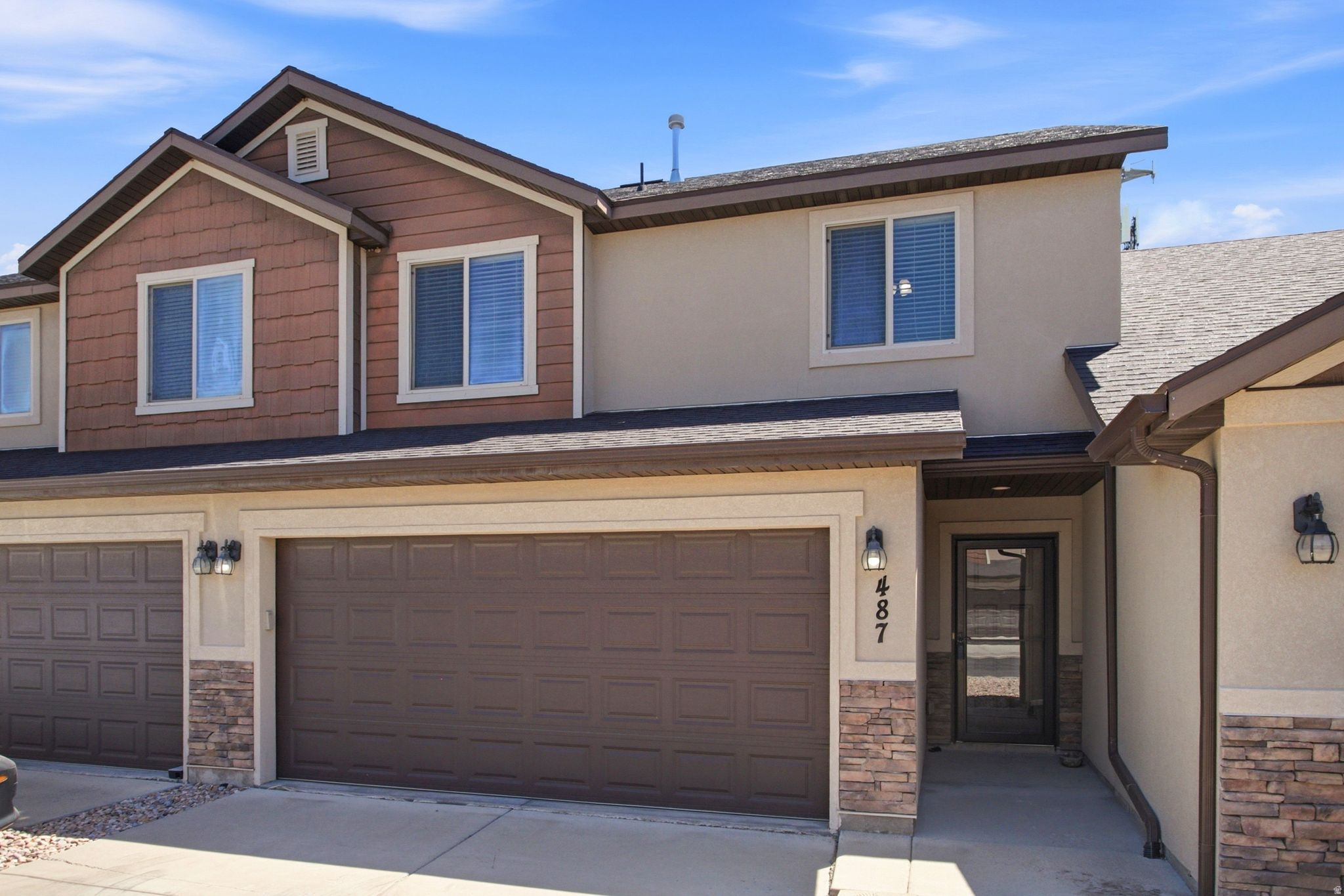 Multi-level townhouse exterior featuring a two-car garage, stacked stone accents, and a covered entry