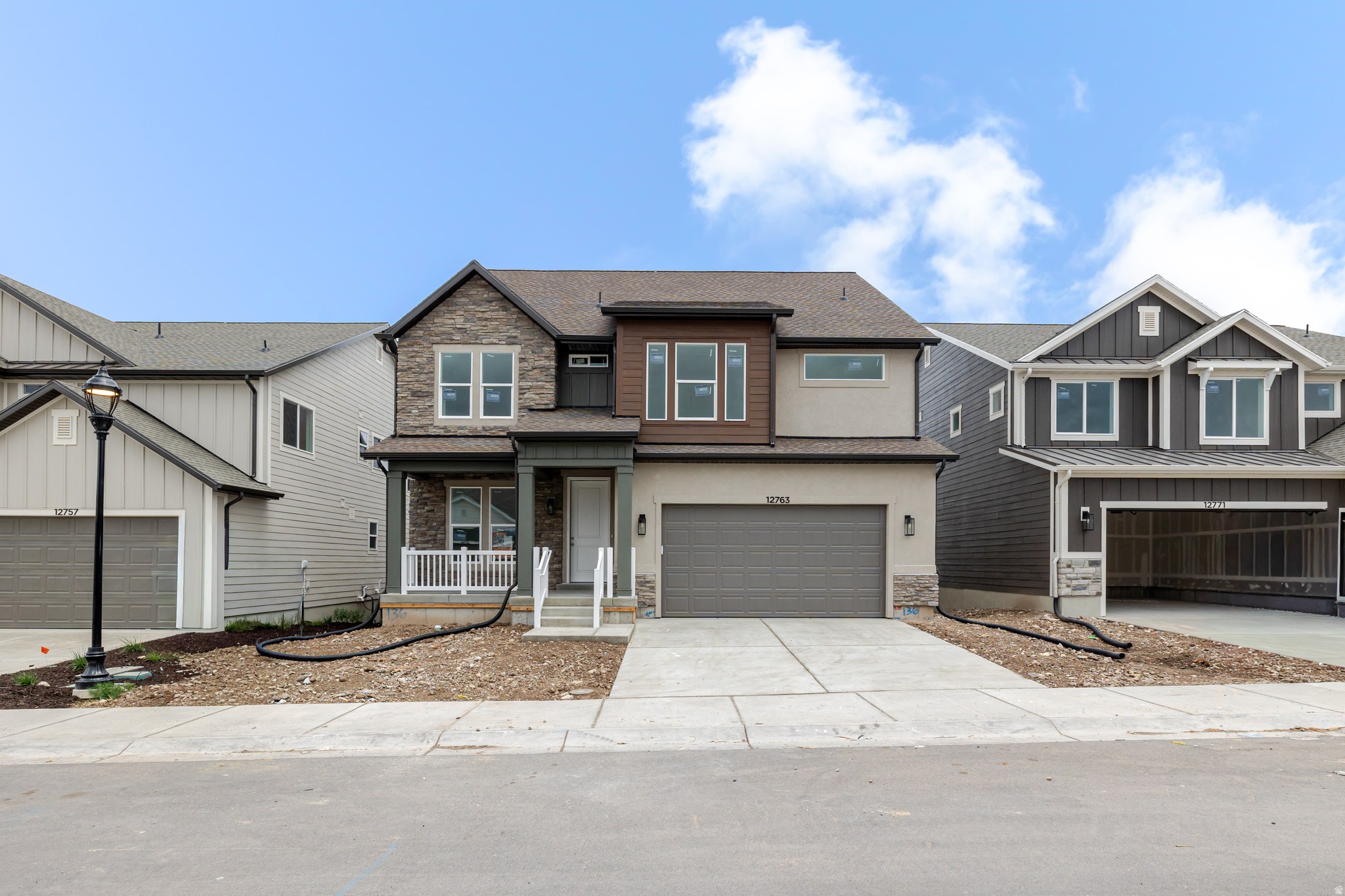 Contemporary-style home featuring a stone and stucco facade, a covered front porch with white railing, and an attached two-car garage