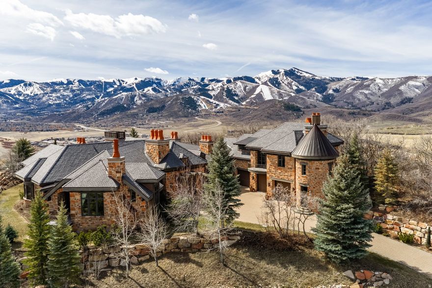 Join us for launch event on Wednesday, March 25th from 12pm to 3pm. This beautifully constructed mountain estate sits just beyond the gates of Glenwild, perfectly positioned on 1.8 acres with sweeping views of Deer Valley Resort and the esteemed Glenwild Golf Course. Designed by Michael Upwall, this property was inspired by a refined Scottish hunting lodge and embodies a timeless Ralph Lauren aesthetic with rich textures, curated finishes, and impeccable craftsmanship. The grand entry is framed by hand-carved double doors with beveled glass that open to soaring ceilings, dramatic wood beams, statement lighting, and walls of windows perfectly capturing the mountain vistas. Designed for seamless main-level living and both intimate and grand entertaining, the great room centers around a dramatic fireplace with stone surround and herringbone brick, flowing effortlessly into the formal dining space and quiet reading nook. The chef's kitchen serves as the true heart of the home offering abundant prep space, a French La Cornue range, Wolf appliances and generous island seating. Accented by a highly functional butler's pantry ideal for catering or craft space with additional laundry facilities. A secondary living room with stunning leaded glass windows and its own fireplace provides flexibility for formal or informal living tucked away just beyond the kitchen. The executive office is perfectly appointed with oxblood ceilings, wood beams, custom built-ins, brass sconces, a stunning stone fireplace and a rich paisley wall covering creating a regal and dramatic workspace. Retreat to a primary suite that is both generous and serene, featuring custom wood paneling, a custom fireplace, spa-like bath with custom closets that provide ultimate organization and convenience with a hidden washer and dryer. Two additional main-level suites include a second primary option with a private deck, hammered copper soaking tub and stained-glass accents, while the third bedroom offers a charming window seat with built-ins and a thoughtful en suite bath. This property offers incredible cohesion with the surrounding grounds, with nearly every room opening to expansive paver decks designed for lounging, dining, and entertaining, complemented by mature landscaping and a flat lawn yard with panoramic mountain views. Outdoor features include multiple fireplaces, space for an outdoor kitchen, traditional bronze lanterns and copper gutters. Above the three-car garage sits a fully equipped guest residence with vaulted ceilings, full kitchen, dining area, private deck, gas fireplace, clawfoot tub, separate bedroom suite, and a hidden children's bunk nook behind Dutch doors. A cedar sauna and adjacent three-quarter bath add additional luxury. Additional highlights include a heated driveway, large garage with storage and epoxy floors, garage floors. central vacuum, slate-inspired metal and tile roof and thoughtful positioning set back from the road for privacy while maintaining easy gate access. Enjoy the ultimate in privacy and convenience with the guard-gated Glenwild Golf Club lifestyle providing world-class golf, spa, dining, and fitness amenities, all less than 30 minutes from downtown Salt Lake City and the international airport.