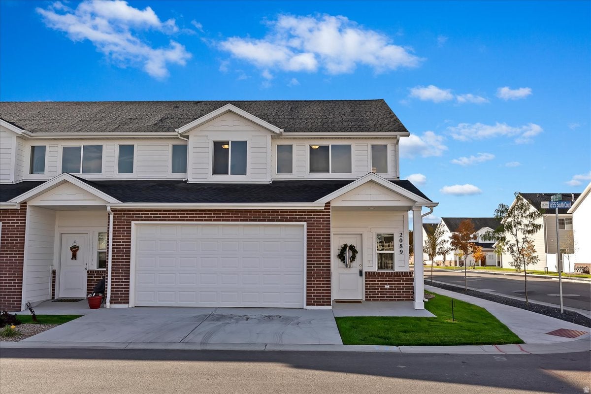 Two-story townhome featuring brick and siding facade, an attached garage, a covered front entry, concrete driveway, and a small lawn area