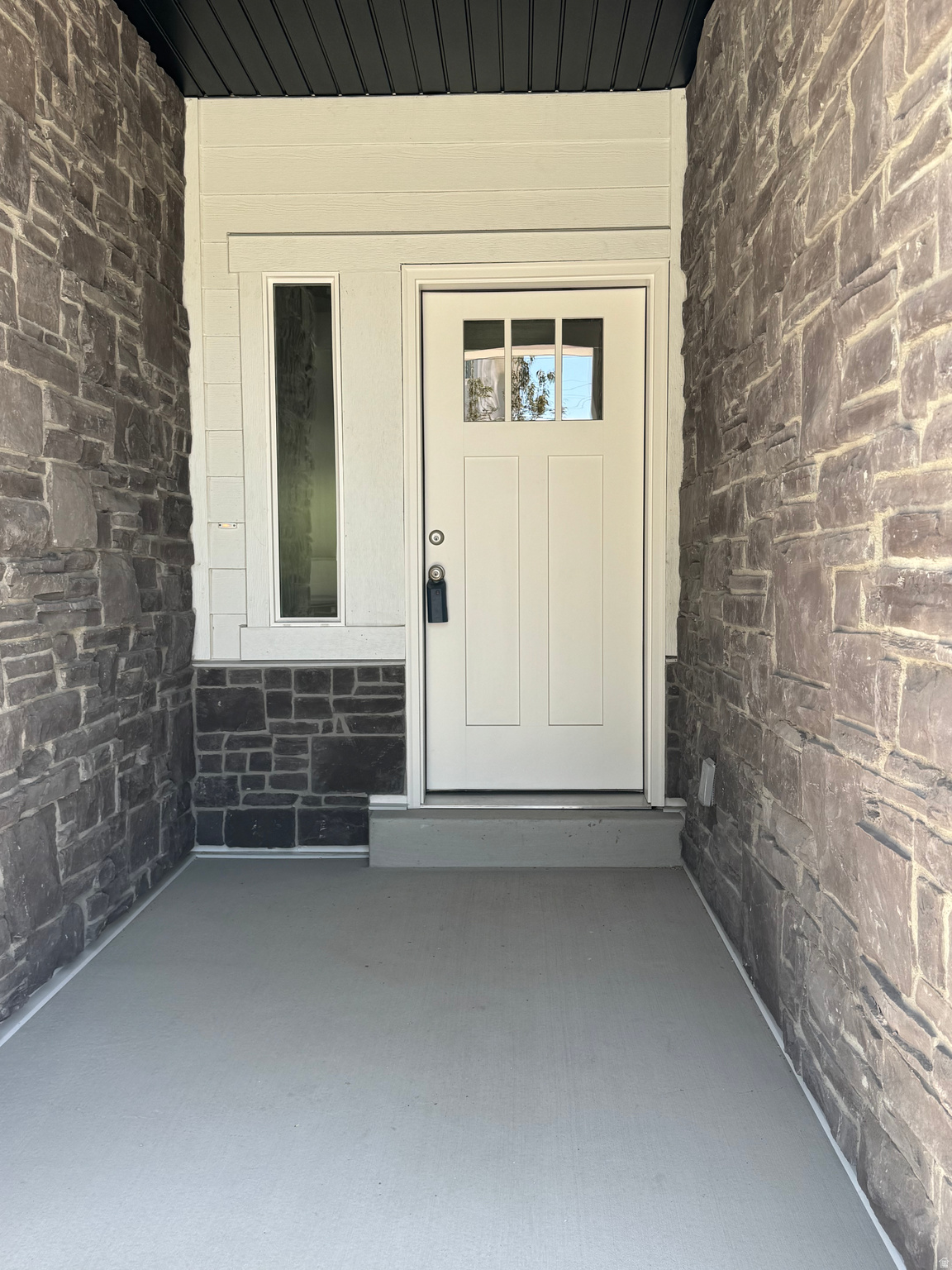 Entryway featuring stone veneer facade, a paneled door with divided lites, an adjacent sidelite, painted siding, and a painted concrete porch