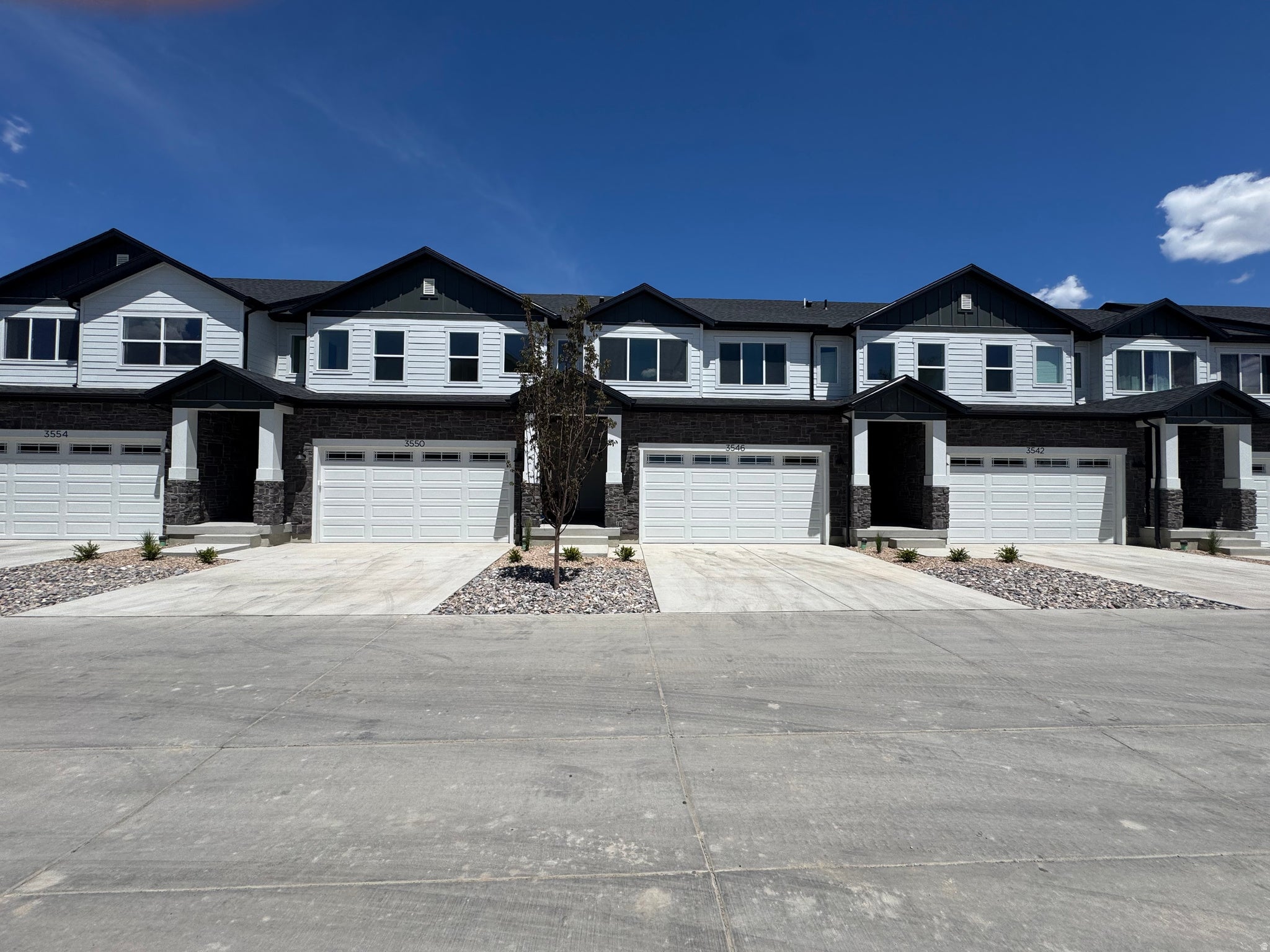 Contemporary multi-level townhome featuring white siding, dark trim, and stone veneer accents