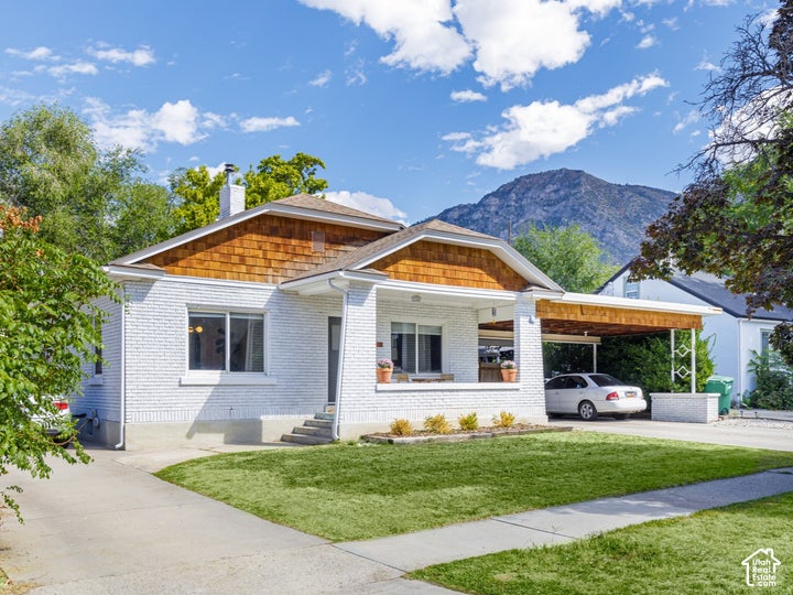 White brick exterior with wood shingle accents, covered front porch, concrete driveway, attached carport, and a mountain…