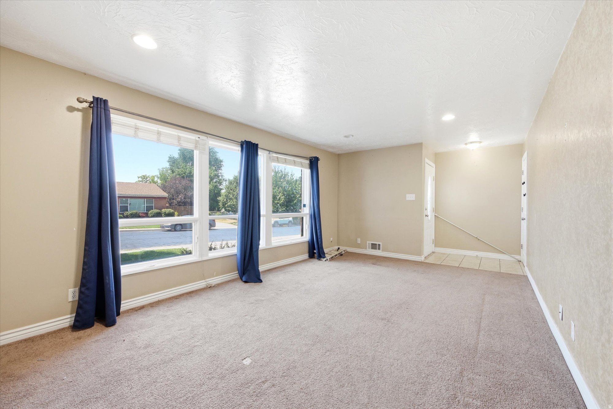 Expansive living area with large picture windows, recessed lighting, neutral tone walls, and soft carpet flooring