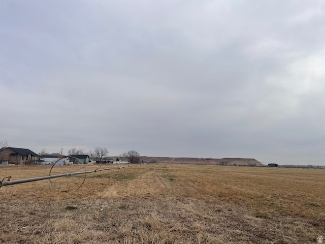 Expansive agricultural land featuring a visible irrigation system and distant structures, framed by a prominent hillside
