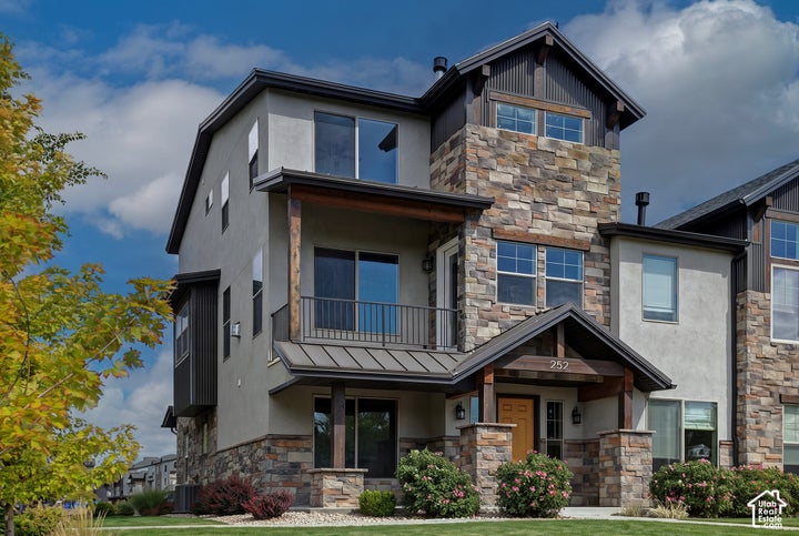 Multi-level exterior featuring stone veneer accents, stucco siding, a metal roof porch covering, a covered balcony with…