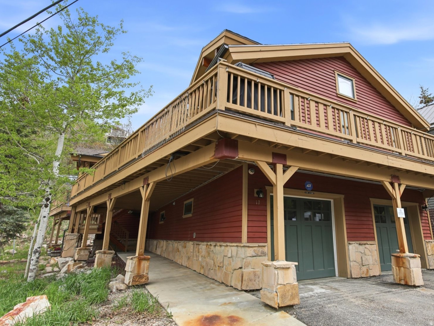 Multi-level property featuring red siding, stone accents, and a prominent second-story balcony with wood railings