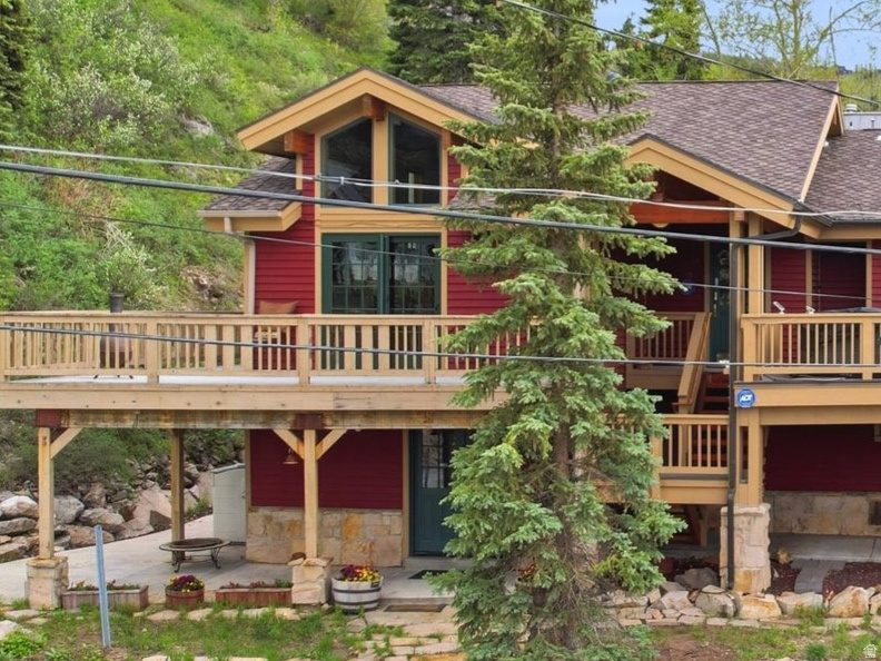 Expansive red-sided residence featuring a full-width upper deck, stone foundation accents, a multi-gabled roofline, and prominent architectural windows