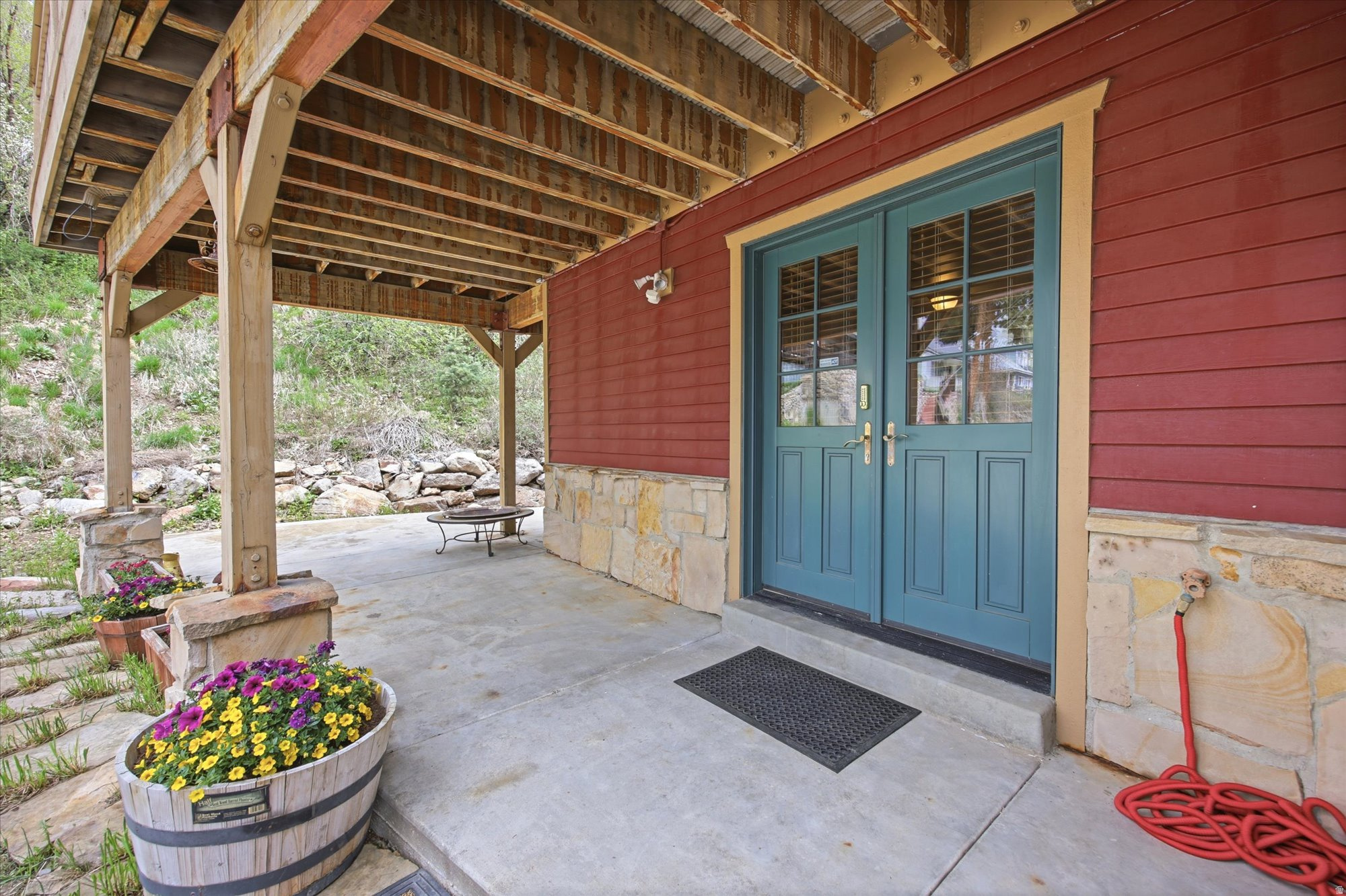 Covered patio featuring exposed wood beams and posts, a concrete surface, stone base accents, and red horizontal siding