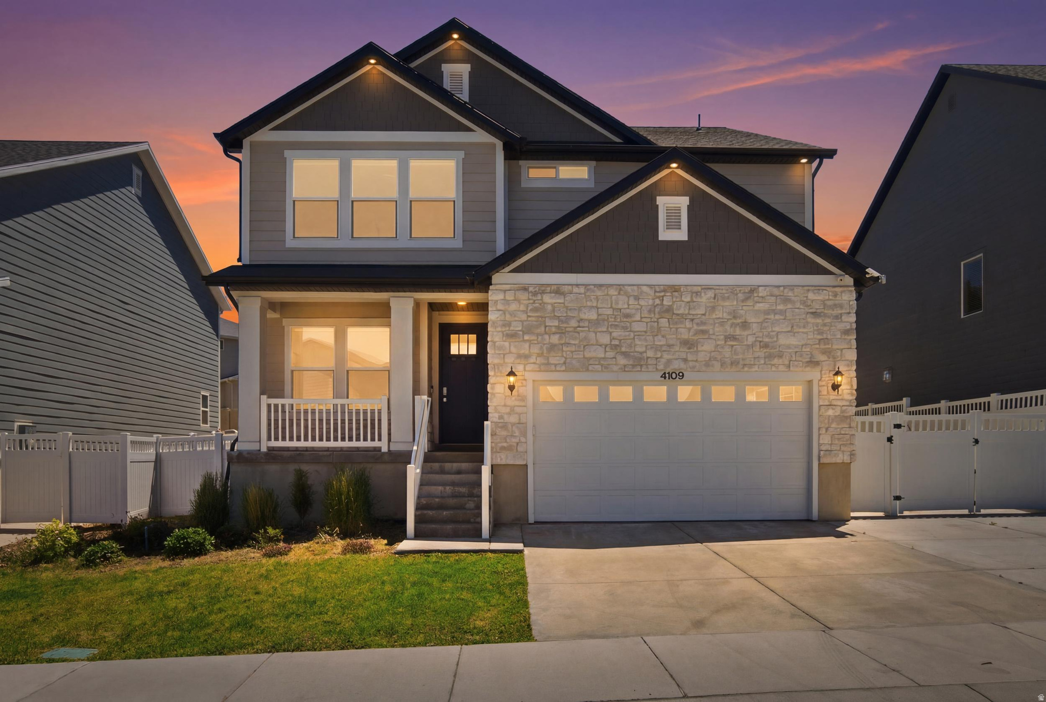 Modern two-story residence featuring a stone and siding exterior, two-car garage with transom windows, covered porch with white railing, and a dark entry door with frosted glass inserts