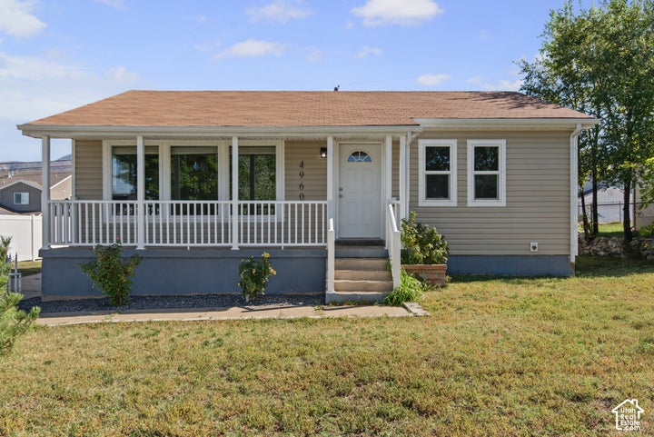 Front exterior featuring tan siding, a covered porch with white railing, a white entry door, and a brown shingle roof