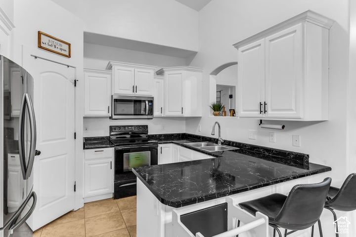 Kitchen featuring white cabinetry, black stone-finish countertops, stainless steel appliances, and a double basin sink