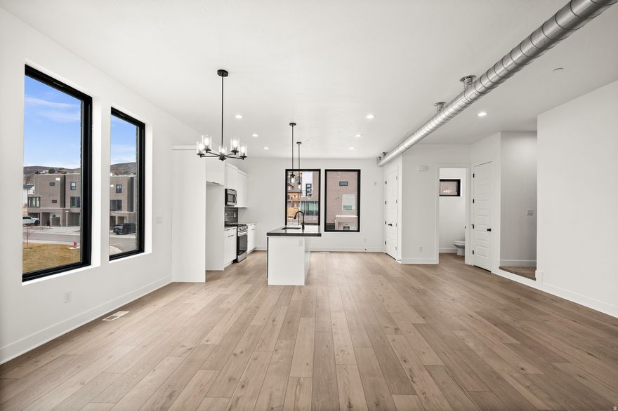 Striking modern design and brand-new construction come together in this 4-bedroom, 3.5-bath end-unit townhome. Clean architectural lines, soaring ceilings, and expansive full-height windows create a light-filled interior, while wide-plank white oak flooring adds warmth and sophistication. The open-concept main level is designed for both everyday living and effortless entertaining. A sleek, contemporary kitchen features high-end custom cabinetry, modern tilework, and stainless appliances, offering a refined yet highly functional workspace. The living area opens to a private balcony, where unobstructed panoramic views showcase the Salt Lake Valley, evening city lights, and remarkable sunsets. Upstairs, the primary suite offers a quiet retreat with its own private balcony, a spa-inspired bath, and generous closet space designed with both comfort and organization in mind. Two additional bedrooms with oversized windows share a full bath, and the conveniently located upper-level laundry adds everyday ease. A spacious landing provides flexible space for a home office, reading area, or additional lounge. The lower level features a private ensuite bedroom with a separate entrance-ideal for guests, a home office, fitness space, or potential income opportunity. Thoughtfully designed and beautifully executed, this home offers a rare combination of modern architecture, functional living spaces, and exceptional natural light. The location provides easy access to nearby trails and parks, as well as shopping, dining, and commuter routes-offering a lifestyle that blends outdoor access with everyday convenience.