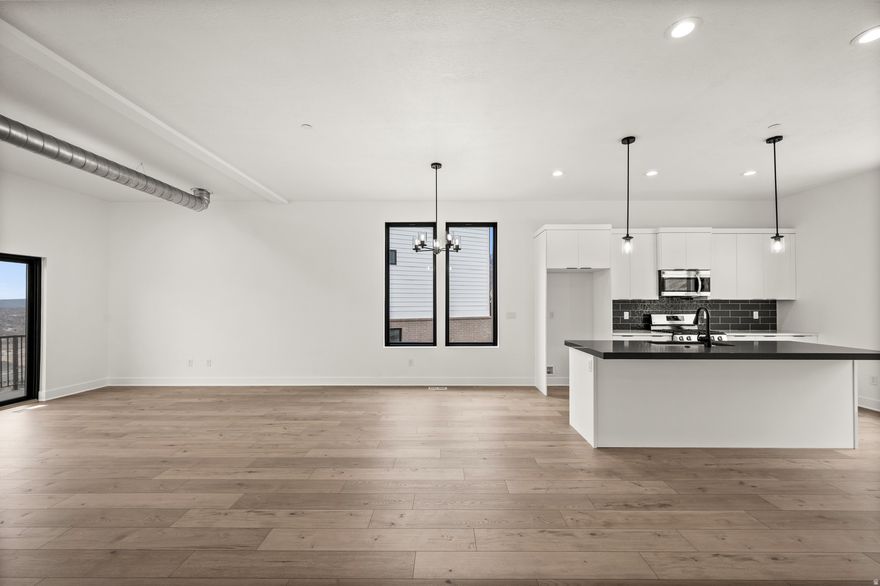 Striking modern design and brand-new construction come together in this 4-bedroom, 3.5-bath end-unit townhome. Clean architectural lines, soaring ceilings, and expansive full-height windows create a light-filled interior, while wide-plank white oak flooring adds warmth and sophistication. The open-concept main level is designed for both everyday living and effortless entertaining. A sleek, contemporary kitchen features high-end custom cabinetry, modern tilework, and stainless appliances, offering a refined yet highly functional workspace. The living area opens to a private balcony, where unobstructed panoramic views showcase the Salt Lake Valley, evening city lights, and remarkable sunsets. Upstairs, the primary suite offers a quiet retreat with its own private balcony, a spa-inspired bath, and generous closet space designed with both comfort and organization in mind. Two additional bedrooms with oversized windows share a full bath, and the conveniently located upper-level laundry adds everyday ease. A spacious landing provides flexible space for a home office, reading area, or additional lounge. The lower level features a private ensuite bedroom with a separate entrance-ideal for guests, a home office, fitness space, or potential income opportunity. Thoughtfully designed and beautifully executed, this home offers a rare combination of modern architecture, functional living spaces, and exceptional natural light. The location provides easy access to nearby trails and parks, as well as shopping, dining, and commuter routes-offering a lifestyle that blends outdoor access with everyday convenience.