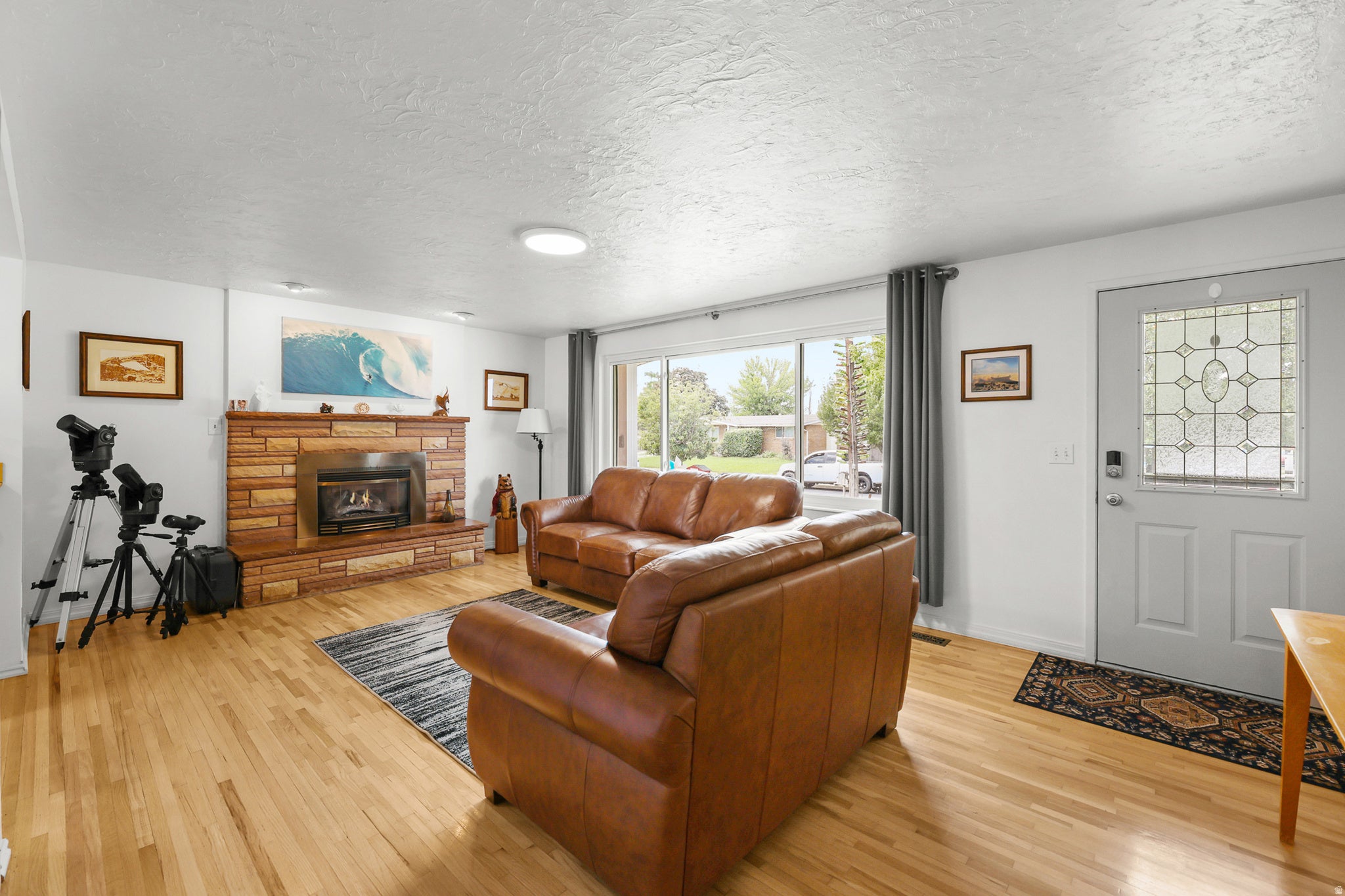 Hardwood flooring, stone fireplace, and large picture window create a bright, inviting gathering space.