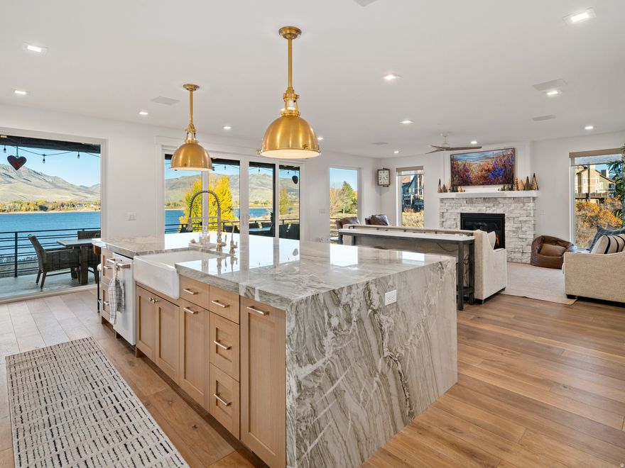 Welcome to an extraordinary lakefront retreat - where design, craftsmanship, and location converge to create a truly exceptional living experience. Every detail of this home was thoughtfully curated to embrace its breathtaking setting. Expansive windows frame lake and mountain views, flooding the interior with natural light and connecting the indoors seamlessly with nature. The main living area showcases a bright, open floor plan anchored by a custom stone fireplace and a chef's kitchen that blends elegance with function. A statement marble island, professional-grade appliances, and striking brass fixtures create a luxurious yet inviting space for entertaining. Sliding glass doors open to a covered patio overlooking the water - perfect for sunset dinners, quiet mornings, or gatherings with family and friends. Upstairs, the serene primary suite captures spectacular sunrise views and features a spa bathroom with marble finishes and a glass-enclosed shower. Each guest room is designed for comfort, style, and privacy. The lower level offers a second full kitchen, ideal for multi-generational living, hosting guests, or creating a private suite. Thoughtful details continue throughout - from the spa-inspired baths with heated floors to the well-appointed laundry and mudroom spaces. With direct lake access, a 2-car garage, zoned for vacation rental and unmatched views in every direction, this home offers both sophistication and serenity - the best of lakeside luxury living.  All property information, boundaries and documents to be verified by buyer.