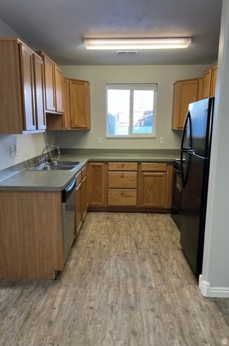 U-shaped kitchen featuring wood-finish cabinetry, light-toned countertops, a stainless steel sink, and wood-finish flooring