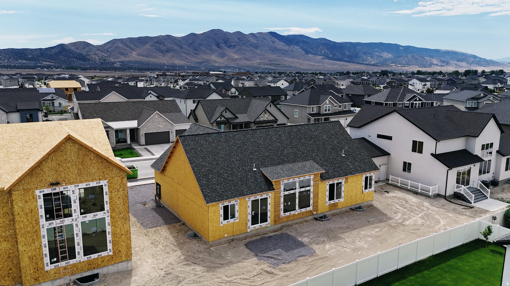 New construction home featuring a dark shingle roof, multiple window styles, and a partially fenced lot