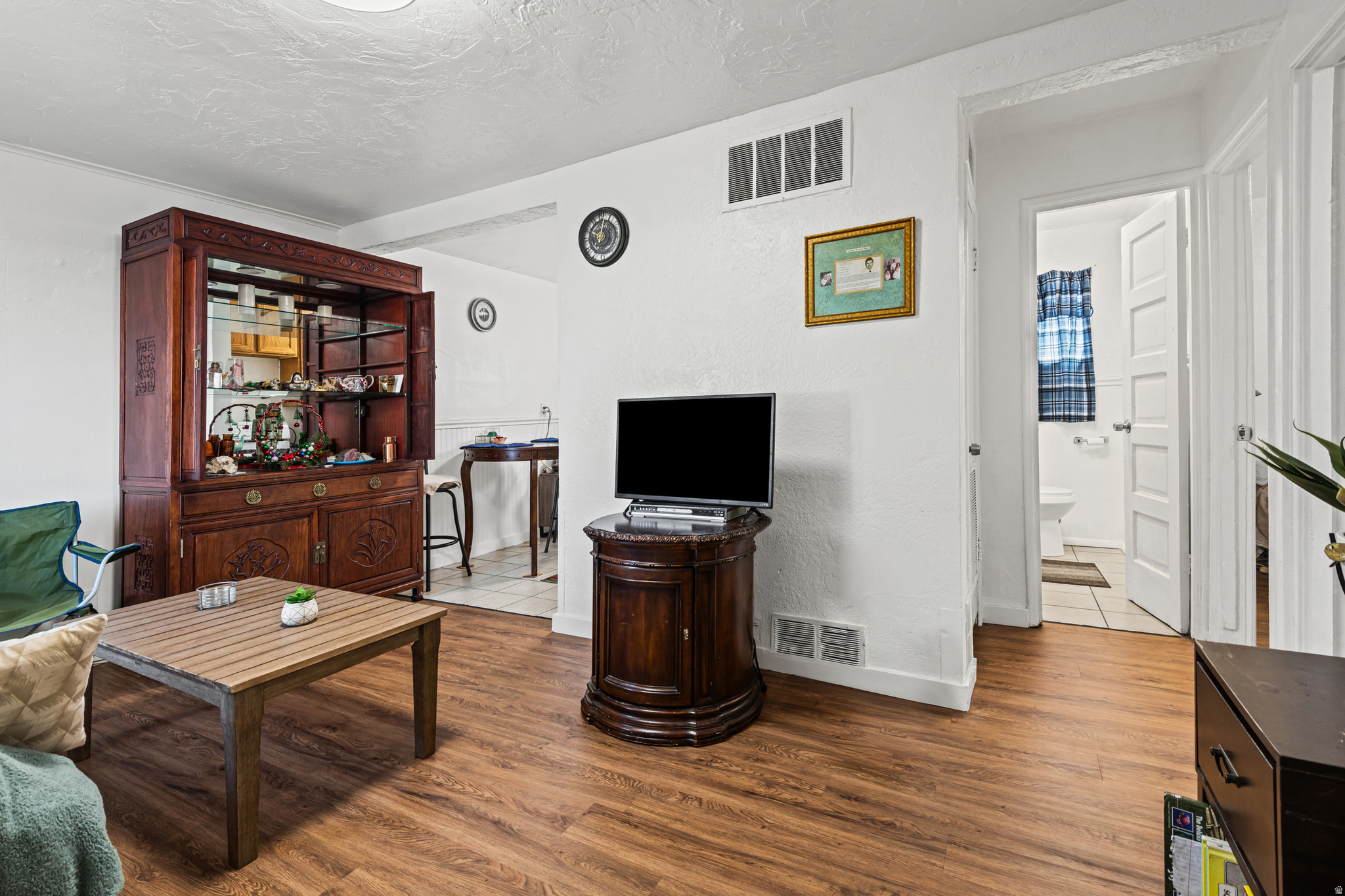 Open-concept living space featuring wood-finish flooring, white walls, and a visible doorway to a bathroom with tiled flooring