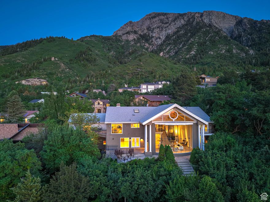 Perched against the Wasatch Mountains and tucked beneath iconic Mount Olympus, this residence offers a unique blend of mountain calm and expansive city views. Upgraded, modernized, and meticulously maintained by its current owners, this 5 bedroom, 5 bathroom home invites you to experience comfortable living with well-designed details throughout. Outside, the home is elegantly understated. Inside, vaulted ceilings, expanses of natural light, and a striking grand room and staircase provide a sense of openness and flow, creating the perfect place to entertain or enjoy a quiet night in. One of the home's standout features is a 27-foot frameless glass wall that captures uninterrupted vistas of downtown, Salt Lake City and the valley below. Other features include a spacious 4-car attached garage, four fireplaces, a private yard, plenty of storage space, and many energy-efficient upgrades throughout. Living here is like being held in the arms of the Wasatch-bathed in breathtaking scenery, while keeping every city convenience just minutes away. Located mere moments from freeway access, the new Salt Lake International Airport, downtown Salt Lake City, Park City, and 6 world-class ski resorts, this is mountain living without compromise. Discover a life that's at once grounded in nature and elevated in every sense.