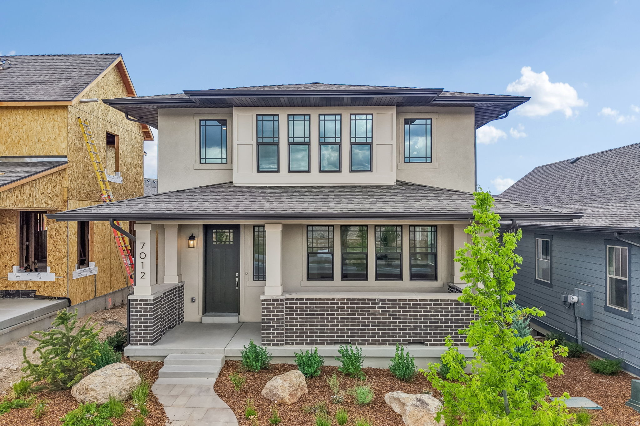 Contemporary architectural facade featuring a covered front porch, dark brick accents, and a dark asphalt shingle roof