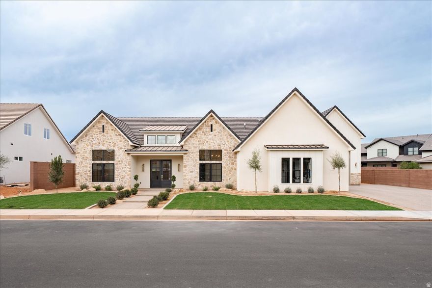 Welcome to a one-of-a-kind custom luxury home where timeless architecture meets modern sophistication. Located in one of Southern Utah's most sought-after communities, this brand-new residence is crafted with premium materials, thoughtful design, and an effortless flow that elevates daily living. From the moment you arrive, the home exudes presence. Stone accents, clean lines, a spacious 3-car garage plus RV garage, and meticulous curb appeal set the tone for what's inside. Step through the 8 ft front door and into a grand foyer with an arched ceiling, designer lighting, and exposed beams that immediately showcase the craftsmanship of this home. The open-concept great room features wide-plank hardwood flooring, expansive sliders for seamless indoor-outdoor living, and a striking chandelier that defines the dining space. Natural light pours through every window, creating a warm and inviting atmosphere. The heart of the home is the gourmet chef's kitchen, complete with a massive Taj Mahal quartz island, custom inset cherry wood cabinetry, brass fixtures, designer pendants, and a built in Frigidaire fridge and freezer. The nearby butler pantry offers abundant storage, display shelving, and additional prep space for entertaining and staying organized. Retreat to the luxurious primary suite, where tall windows, soft natural light, and calming finishes set the scene for relaxation. The spa-inspired ensuite features an extended double vanity, custom mirrors, brass lighting, a walk-in shower with built-in niches, and beautiful tile craftsmanship. Two additional guest bedrooms include designer lighting, double-door closets, and crisp finishes, all just steps away from an elegant full bathroom featuring custom tilework and a deep soaking tub. The half bath near the foyer adds another touch of luxury with custom cabinets and statement sconces. The laundry and mudroom are spacious and stylish, offering checkerboard tile flooring, ample cabinetry, a deep sink, and convenient access points to the garage and living areas. Beyond the glass, the covered patio provides year-round enjoyment with recessed lighting and plenty of room for outdoor dining or lounge seating. The private backyard features low-maintenance desert landscaping and walking distance to Zion Shores surf park. Be sure to check out Zion Shores on the web. The largest wave park in the US coming in 2027 to this neighborhood.