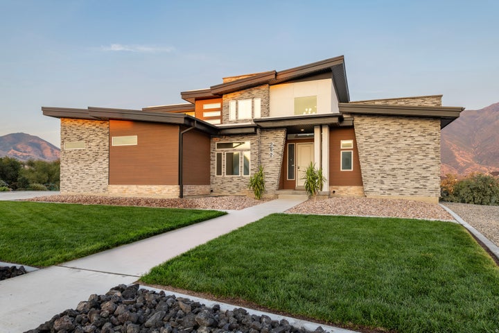 Modern architectural exterior with a multi-level roofline, stone veneer and wood-finish siding, a concrete pathway, and…