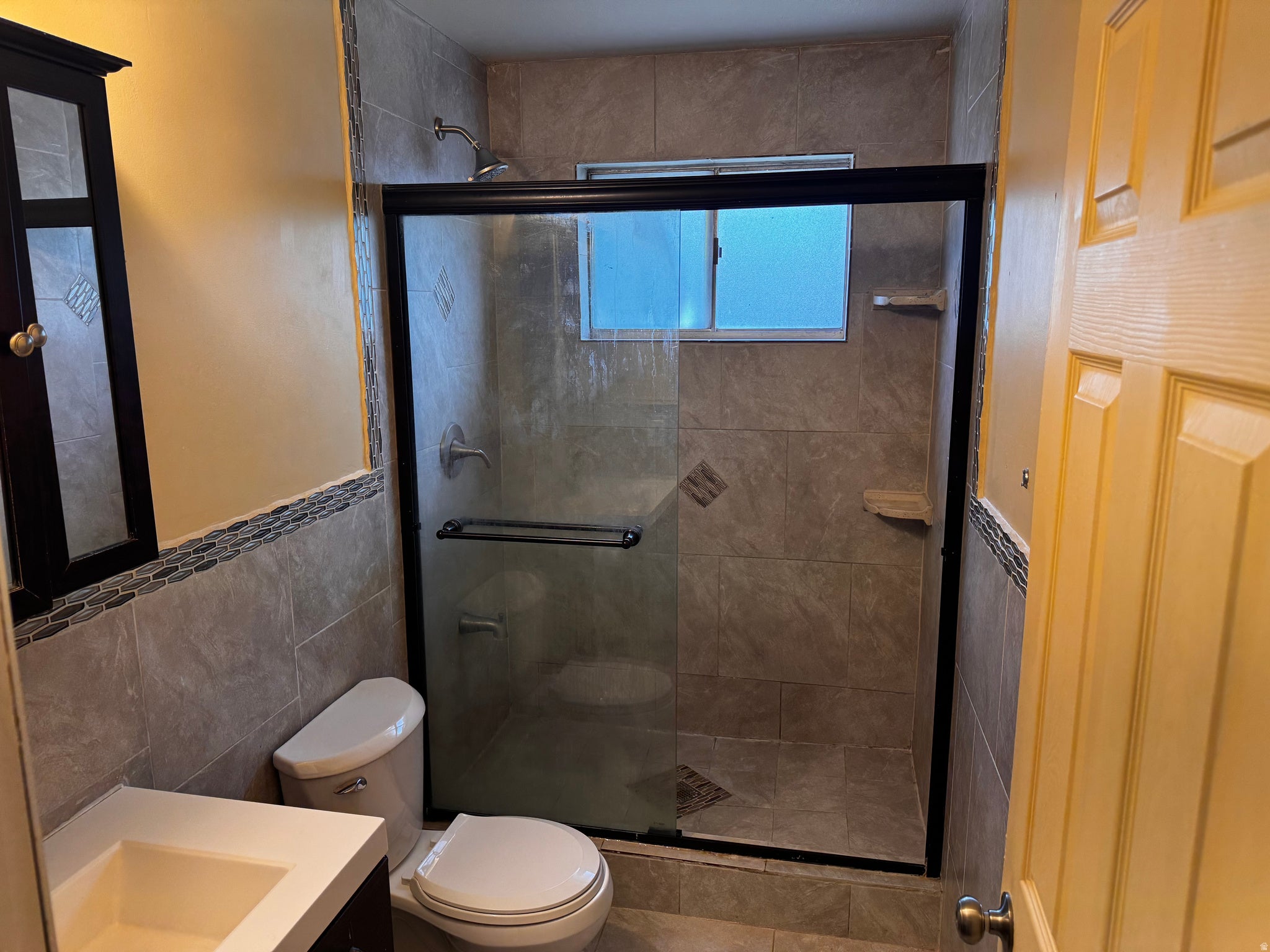 Tile-surrounded shower with glass enclosure, integrated shelving, and window