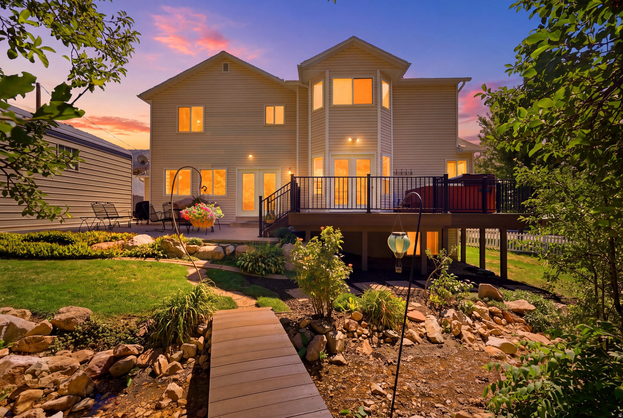 Spacious rear exterior with a multi-level deck, ground-level patio, and a wood-finish footbridge over a rock garden